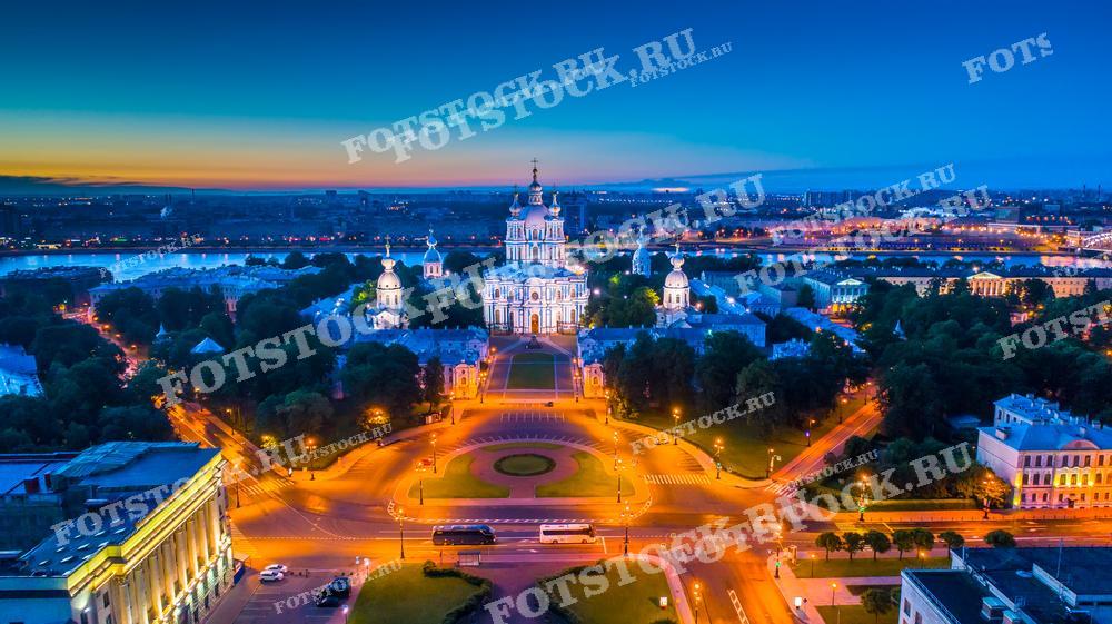 Фотография демонстрирует Смольный собор, один из архитектурных символов Санкт-Петербурга. Собор освещён и величественно возвышается над окружающей застройкой, подчеркивая его историческое и культурное значение. Этот снимок идеален для использования в публикациях, посвящённых религиозной архитектуре и ночной фотографии городских ландшафтов.